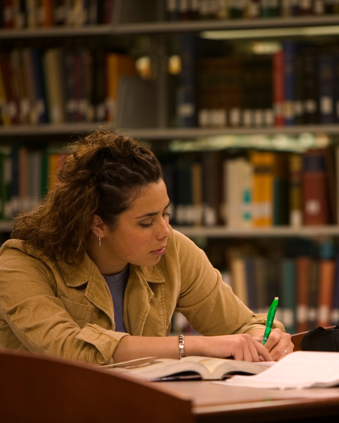 Una joven en la biblioteca está escribiendo en un libro con un bolígrafo verde.